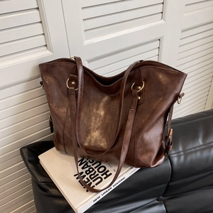 Deep brown large capacity faux leather tote bag with gold hardware on a leather sofa
