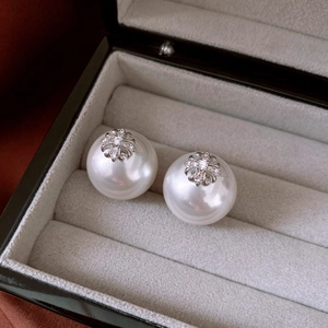 Macro shot of silver pearl earrings with luxury cross detail in a black jewelry box