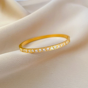 Macro detail of gold-plated bangle with sparkling circular zircons on beige silk