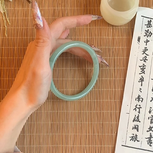 Traditional Chinese style light green glass bangle on bamboo mat with scroll background