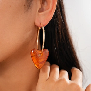 Close-up of heart-shaped amber acrylic charm on golden hoop earring worn by a model