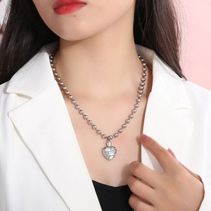 Close-up of silver heart-shaped urn locket on a delicate ball chain necklace