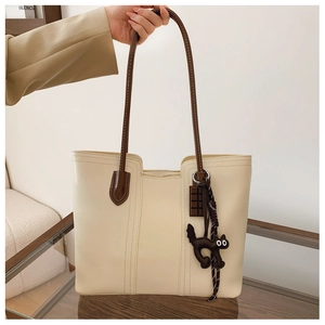 Detail of a cream tote bag with brown straps and cute cat and chocolate charms