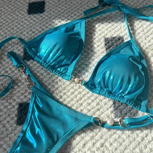 Detail of metallic peacock blue bikini featuring elegant faux pearls and gold hardware
