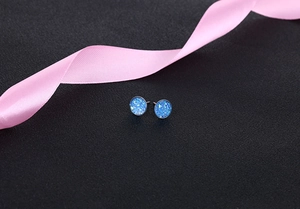 Macro shot of 10mm round blue crystal stud earrings on black leather with pink ribbon