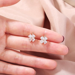 Macro shot of gold four-leaf clover stud earrings with heart-shaped white zircon stones
