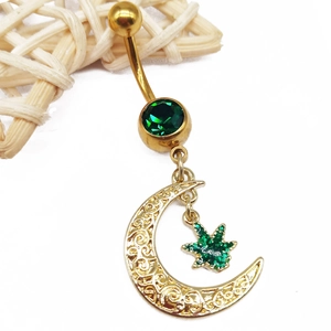 Gold moon and star belly button ring with green gemstone dangling on a white background