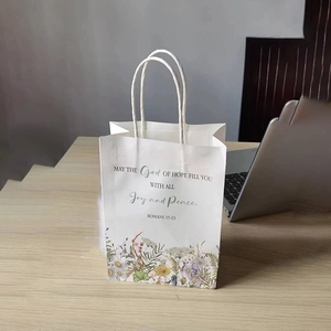 Detail of white paper gift bag featuring floral illustration and religious quote on a wood desk