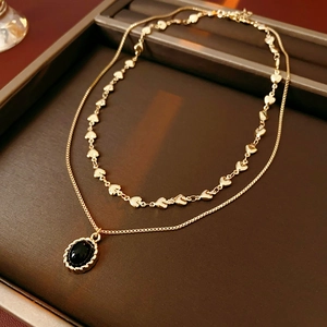 Detail of gold double-layer necklace featuring a heart chain and black oval gemstone pendant