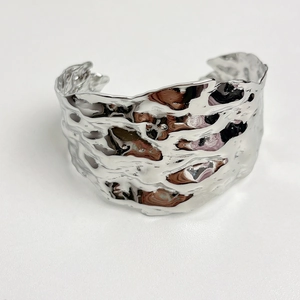 Macro view of wide silver metal bracelet with irregular lava texture and open C shape