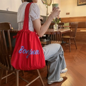 Detail of red canvas tote bag with blue Bonjour slogan in a vintage cafe setting