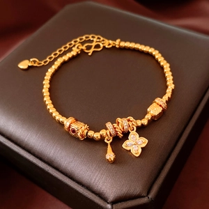 Detail of 24K gold-plated beaded bracelet with floral charms on a jewelry box