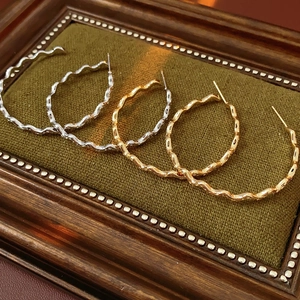 Detailed close-up of wavy gold and silver C-shaped hoop earrings on green velvet