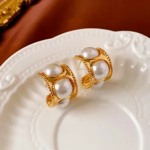 Vintage golden C-shaped hoop earrings with white pearls on elegant white ceramic plate