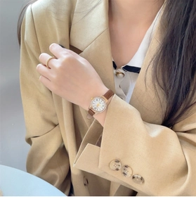 Close-up of elegant women's watch with gold diamond case and brown leather strap on wrist