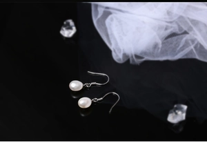 Macro detail of natural white pearl earrings with silver hooks on a black mirrored base