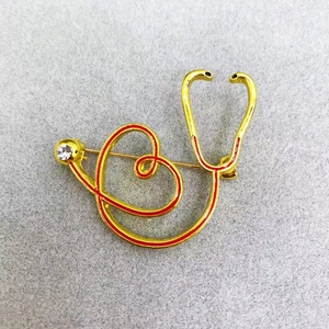 Detail of gold stethoscope brooch with red enamel lines and a sparkling crystal accent
