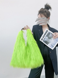 Detail of neon green long faux fur tote bag with black strap held by a model