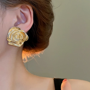 Dettaglio di grandi orecchini a rosa dorata con petali metallici e finitura lucida