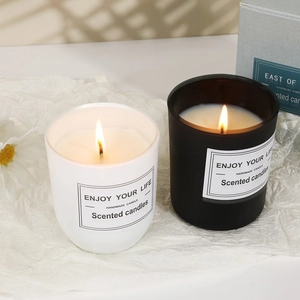 Black and white scented candles lit in glass jars on a soft white background
