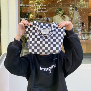 Corduroy draagtas met schaakbordpatroon en label, vastgehouden door model in een hippe café-omgeving
