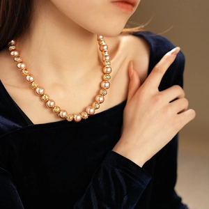 Close-up of a necklace with hollow gold beads and champagne pearls on a model's neck