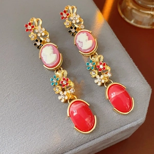 Close-up of vintage gold earrings with floral enamel, cameo portraits and red gemstones