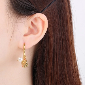 Close-up of golden heart hoop earring with pearl and red tassel on a female model