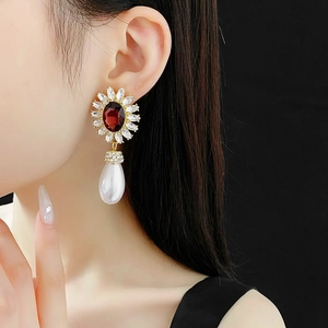 Close-up of vintage gold earrings with red oval gemstone and drop pearl on model