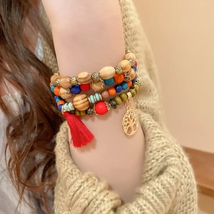 Detail of layered bohemian sandalwood bracelet with tree of life charm and red tassel