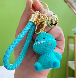 Detailed view of blue resin dinosaur keychain with woven strap and golden bell charm
