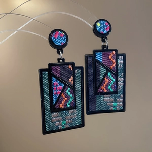 Detailed close-up of geometric embroidered rectangular drop earrings with colorful patterns