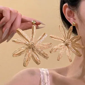 Gros plan de boucles d'oreilles fleurs en raphia tissé avec détails dorés