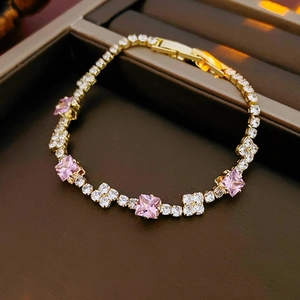 Macro detail of gold bracelet featuring pink square zircons and star-shaped white crystals