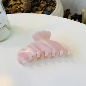 Close-up of pink marble pattern acetate hair claw clip on a white table with green plants