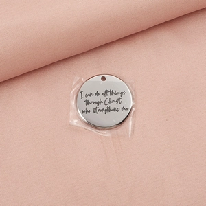 Close-up of a round stainless steel charm engraved with inspirational Bible verse text