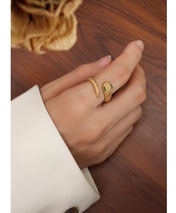 Detail of snake-shaped ring in 18k gold plating with green gem eyes on hand