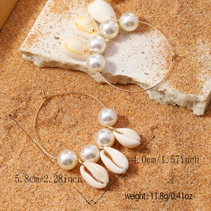 Bohemian gold hoop earrings with white pearls and natural cowrie shell pendants on sand