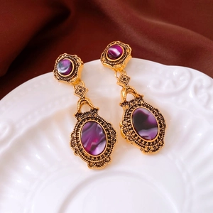 Close-up of vintage gold earrings with purple stones on an elegant embossed porcelain dish