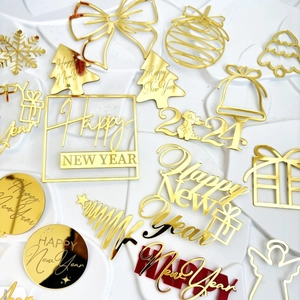 Golden acrylic Christmas and 2024 New Year cake topper set on a white textured surface