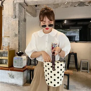 Detail of a vintage polka dot canvas bucket bag held by a model in casual outfit