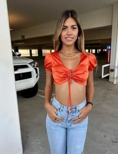 Détail du crop top en satin orange avec col en V à cordon et manches bouffantes