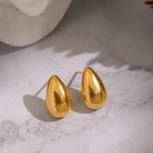 Macro detail of gold teardrop earrings resting on a modern grey marble surface