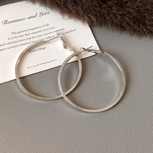 Minimalist large silver hoop earrings with a polished finish on textured background