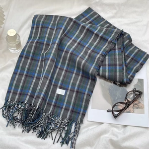 Detail of grey plaid scarf with blue stripes and fringes on a cozy lifestyle background