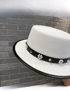 Close-up of woven white boater hat featuring black leather band and pearl flower detail