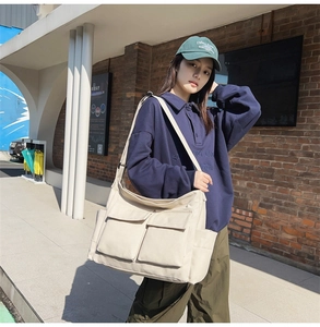 Detail of off-white canvas crossbody bag with multiple pockets and wide strap on model