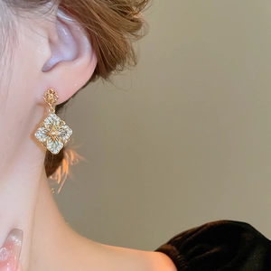 Gros plan de boucles d'oreilles fleur dorées avec émail bleu-vert et zircons sur mannequin