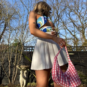 Outdoor low angle shot of floral halter crop top with white pleated mini skirt and plaid bag