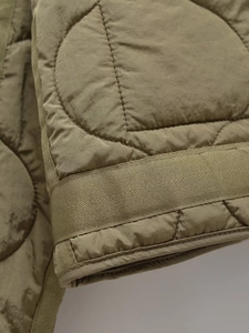 Detail of olive green quilted jacket featuring circle stitching and reinforced woven tape